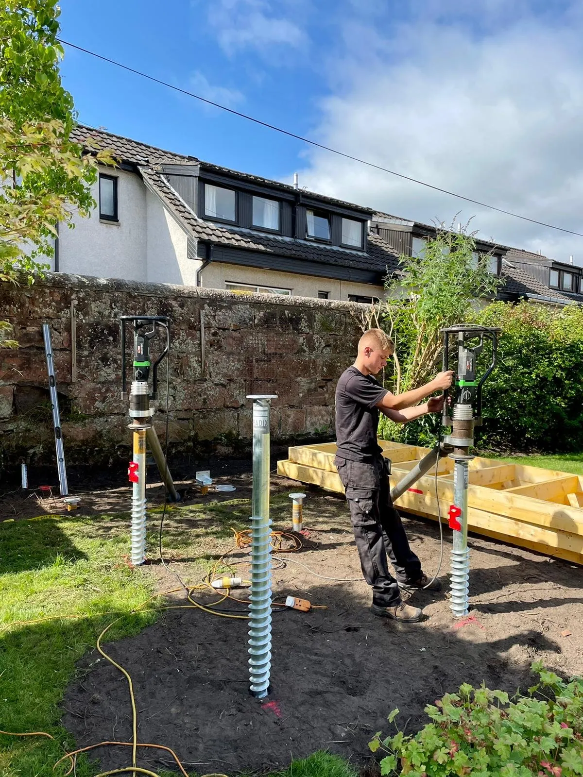 An MW Ground Screws installer driving galvanised ground screws into position with hydraulic drivers on a garden project